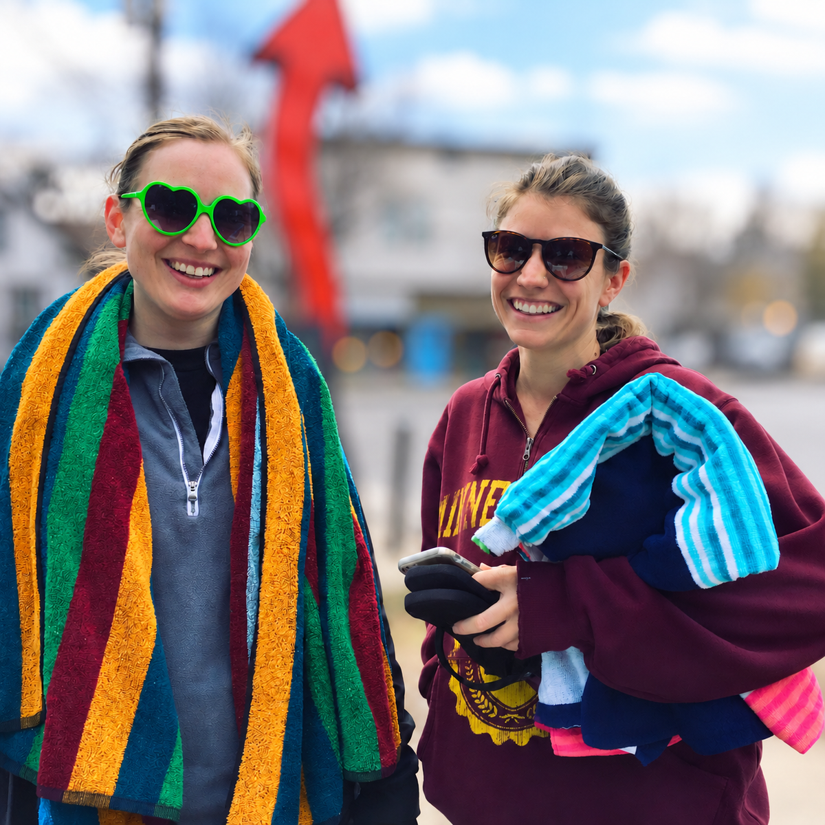 Two smiling bathers with colorful towels against a softly blurred street background